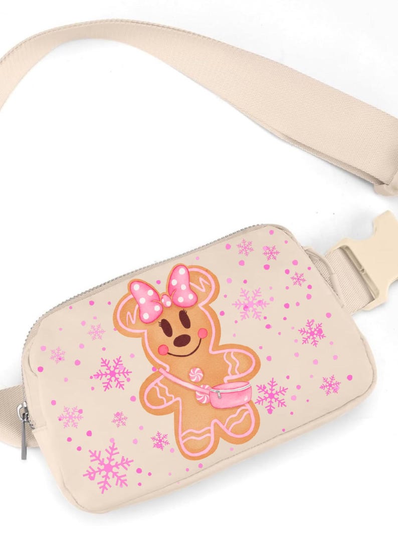 May include: Beige fanny pack with a gingerbread cookie design. The gingerbread character has a pink bow, purse, and is surrounded by pink snowflakes and dots. The strap and buckle are beige.