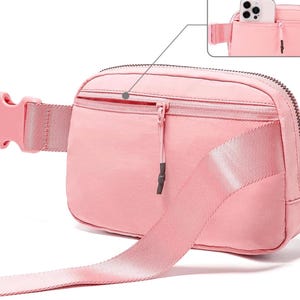 May include: A pink fanny pack with a zippered main compartment and a smaller front pocket. The adjustable strap and buckle are also pink. A close-up shows a phone in the back pocket. The bag is made of a smooth, durable material.