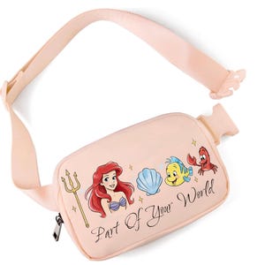 May include: A pale pink fanny pack with a graphic of Ariel, a seashell, Flounder, and Sebastian. The text "Part Of Your World" is printed on the front. The adjustable strap and zipper are black.