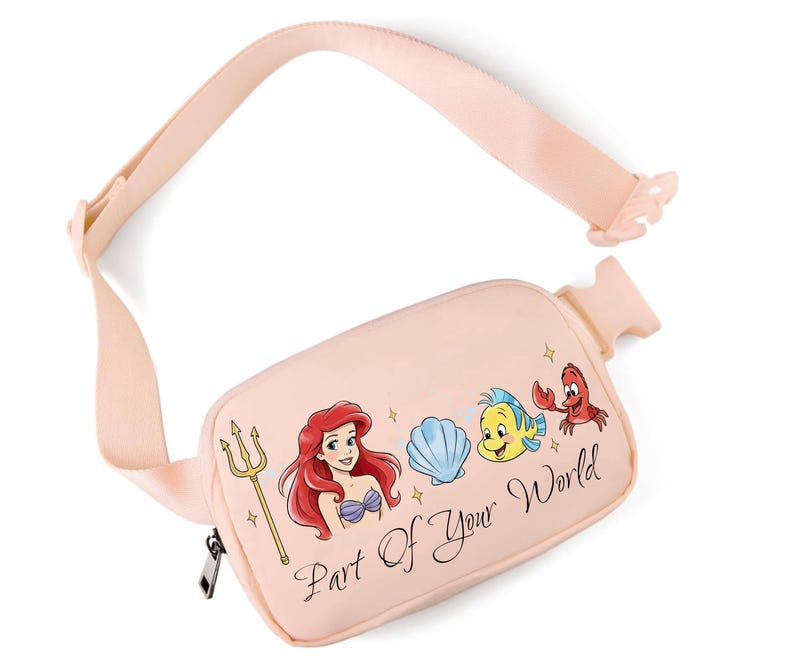 May include: A pale pink fanny pack with a graphic of Ariel, a seashell, Flounder, and Sebastian. The text "Part Of Your World" is printed on the front. The adjustable strap and zipper are black.