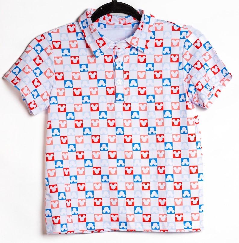 May include: A short-sleeved polo shirt featuring a repeating checkerboard pattern of red, light blue, and white squares. Each square contains a white Mickey Mouse head silhouette. The shirt has a classic collar and a three-button placket front.