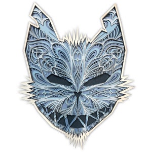 May include: A blue and white intricate laser cut wooden cat mask with a menacing expression. The mask is detailed with a variety of patterns and designs.