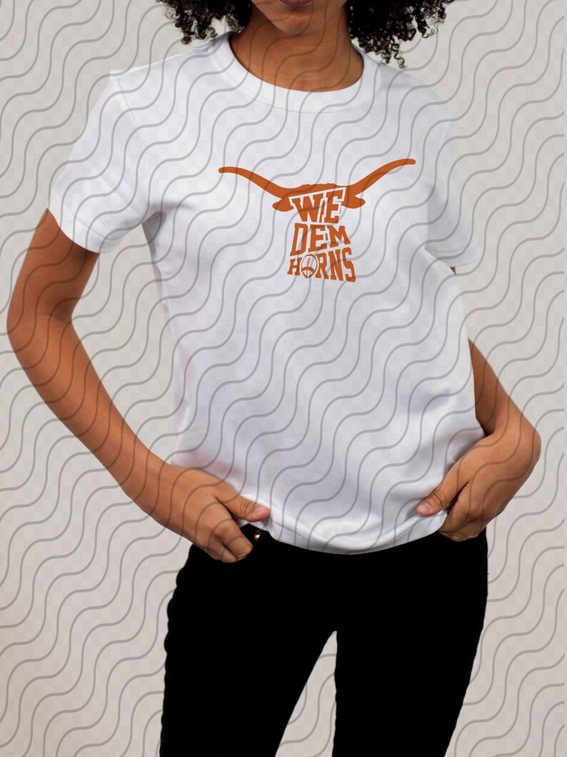 May include: White t-shirt with a brown graphic of a longhorn steer head with the text "We Dem Horns" printed on it.