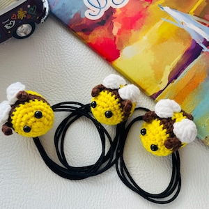 May include: Three crocheted bee hair ties with black elastic bands. The bees are yellow with brown stripes and white wings.