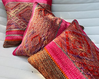 May include: Three decorative throw pillows with vibrant pink, red, and orange woven patterns. The pillows have a square shape and feature intricate designs with a textured appearance. The color palette includes shades of pink, red, orange, and brown.