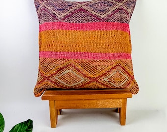 May include: A square throw pillow featuring a woven texture with horizontal bands of orange, hot pink, and deep purple. The top and bottom sections display a repeating diamond pattern in shades of purple, pink, and orange across the fabric surface.