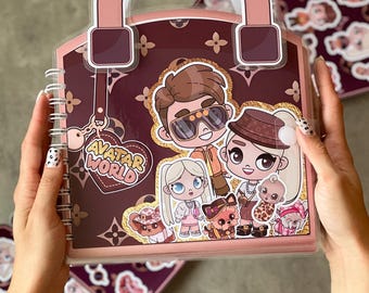 May include: A pink and burgundy scrapbook with a handle, featuring cartoon characters and the text "AVATAR WORLD." The scrapbook has a spiral binding and is decorated with a repeating pattern. Additional sticker sheets are visible.