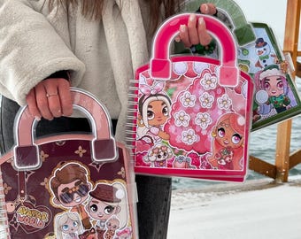 May include: Three colorful notebooks with handles, resembling handbags, are held up. The notebooks feature cartoon illustrations and the text "AVATAR WORLD." The notebooks have pink, green, and brown accents, with spiral binding.