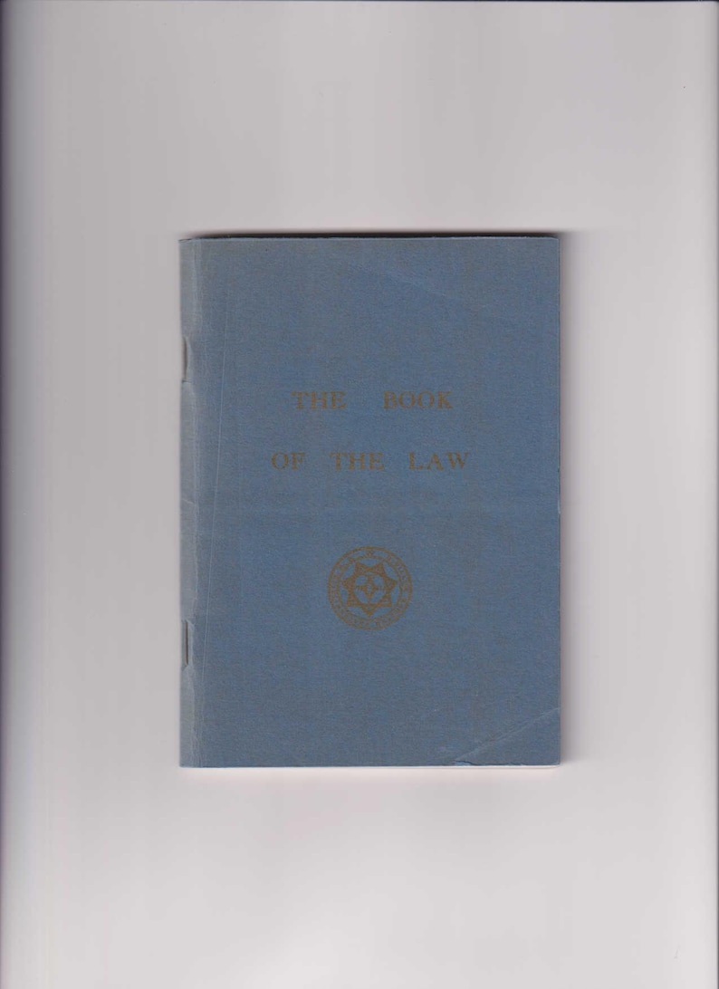 May include: A blue book with the title "The Book of the Law" printed in gold lettering. A gold emblem is centered on the cover.