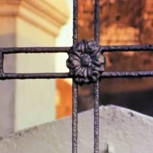 May include: A black metal cross with a decorative flower design in the center.