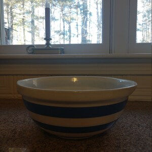 May include: A white mixing bowl with blue stripes. The bowl is made of ceramic and has a smooth, glossy finish.