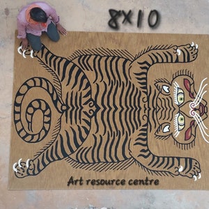 May include: A black and white tiger illustration on a brown wooden background. The tiger is lying on its back with its paws in the air. The text "Art resource centre" is printed below the tiger.