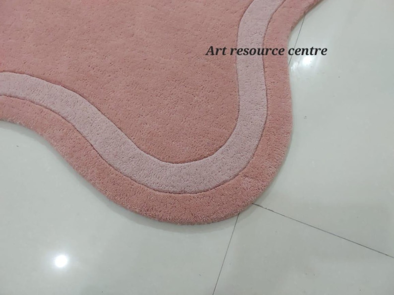 Puede incluir: Primer plano de una alfombra de ba&ntilde;o rosa y blanca con un borde ondulado. La alfombra est&aacute; hecha de un material suave y esponjoso.