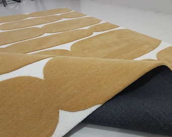 May include: A close-up of a beige and white area rug with a geometric pattern. The rug is folded in half, revealing a dark gray backing.