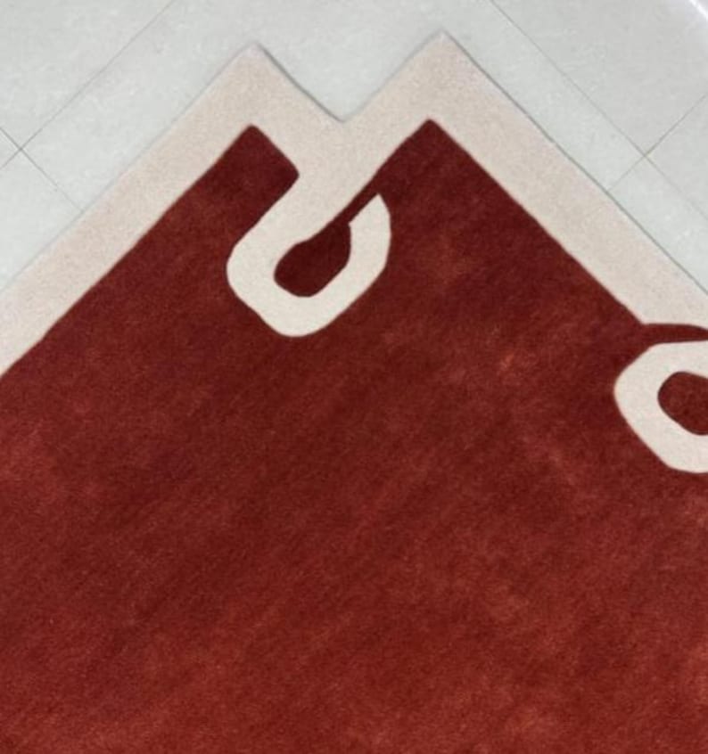 Puede incluir: Una alfombra roja con un borde blanco y un dise&ntilde;o abstracto blanco. El dise&ntilde;o presenta una forma grande y curva que se asemeja a una letra "C".