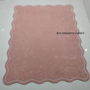 Puede incluir: Una alfombra rosa claro con un borde festoneado y un borde blanco. La alfombra est&aacute; hecha de un material suave y mullido. El texto "Art resource centre" est&aacute; impreso en la esquina superior derecha de la alfombra.