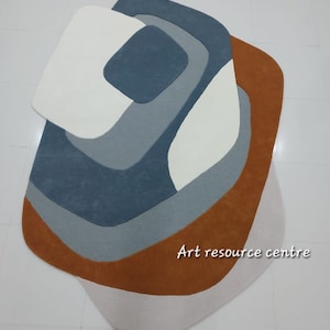 Puede incluir: Alfombra de &aacute;rea abstracta con un dise&ntilde;o geom&eacute;trico en tonos de marr&oacute;n, gris y blanco. La alfombra tiene una forma &uacute;nica y org&aacute;nica.