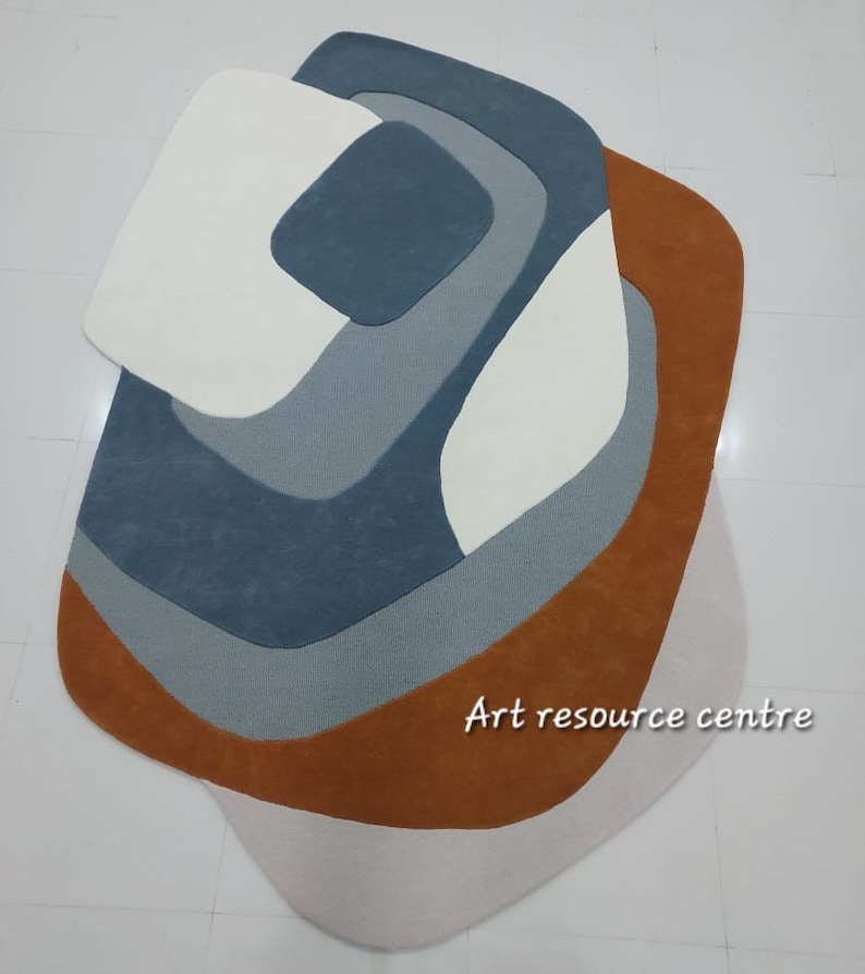 Puede incluir: Alfombra de &aacute;rea abstracta con un dise&ntilde;o geom&eacute;trico en tonos de marr&oacute;n, gris y blanco. La alfombra tiene una forma &uacute;nica y org&aacute;nica.