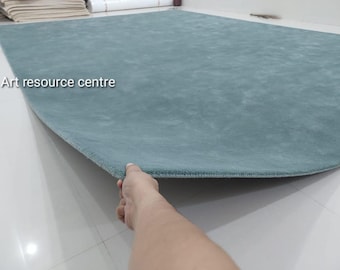 Puede incluir: Una alfombra grande de color verde azulado sólido con una textura suave y afelpada. La alfombra es rectangular con esquinas redondeadas y presenta el texto Art resource centre impreso en blanco en el lado izquierdo de la superficie.