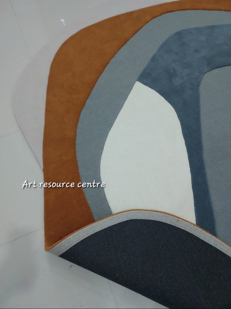 Puede incluir: Primer plano de una alfombra con un dise&ntilde;o geom&eacute;trico en tonos marrones, grises y blancos. La alfombra tiene un respaldo negro y un borde blanco. El texto "Art resource centre" es visible en la esquina inferior izquierda de la imagen.