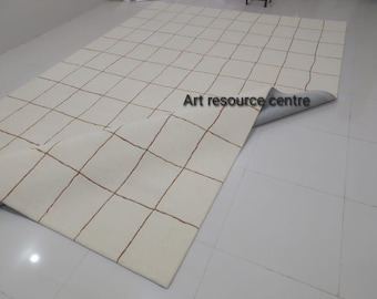 May include: A white rug with a grid pattern of thin brown lines. The rug is folded in half and the underside is visible.