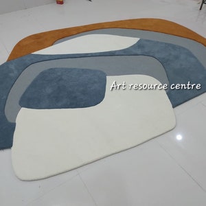 Puede incluir: Alfombra de &aacute;rea abstracta con un dise&ntilde;o blanco, azul claro, azul oscuro y naranja. La alfombra est&aacute; hecha de un material suave y mullido. "Art resource centre" est&aacute; escrito en la alfombra.