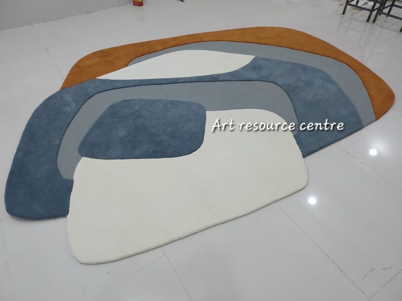 Puede incluir: Alfombra de &aacute;rea abstracta con un dise&ntilde;o blanco, azul claro, azul oscuro y naranja. La alfombra est&aacute; hecha de un material suave y mullido. "Art resource centre" est&aacute; escrito en la alfombra.
