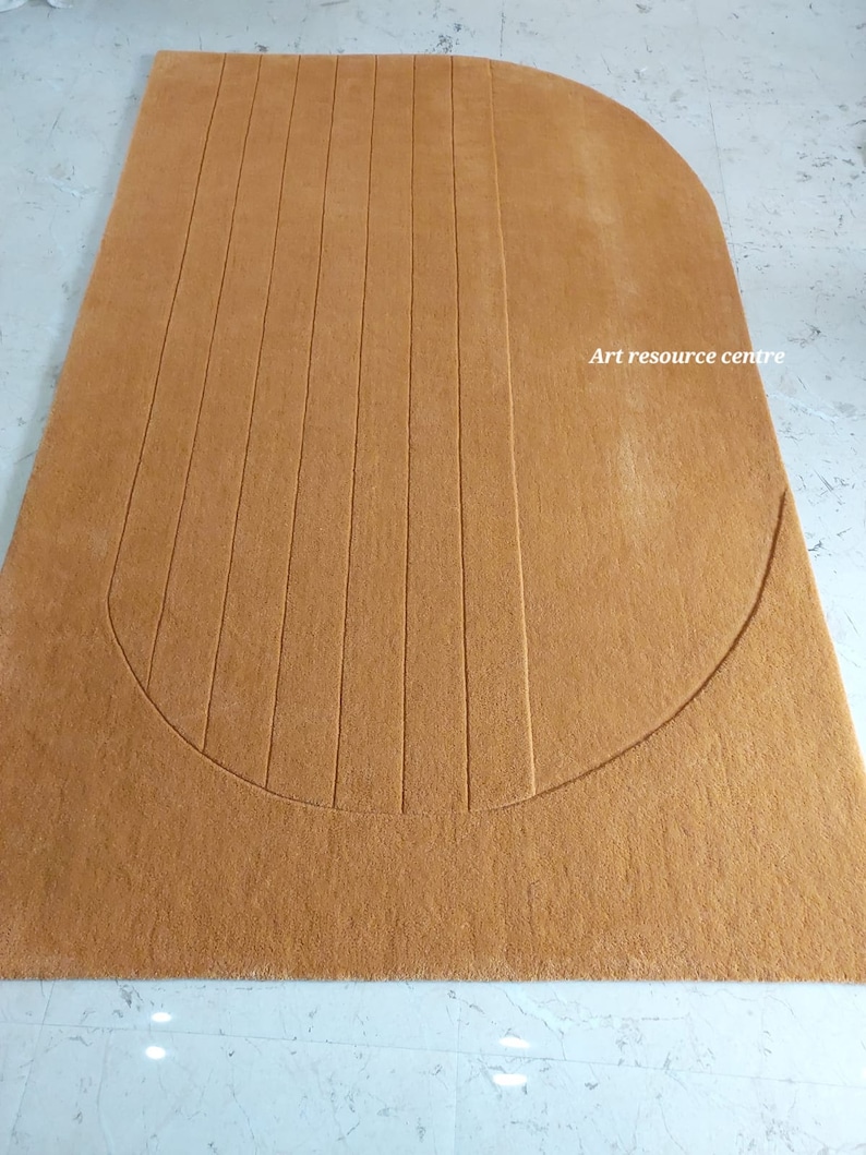 Puede incluir: Una alfombra rectangular de color marr&oacute;n claro con un borde superior redondeado. L&iacute;neas verticales est&aacute;n grabadas en la superficie de la alfombra, creando un patr&oacute;n texturizado. El texto "Art resource centre" est&aacute; impreso.