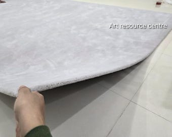 May include: A light grey, rectangular rug with a soft, plush texture. The rug is being lifted to reveal its underside. The text "Art resource centre" is visible on the rug's surface.