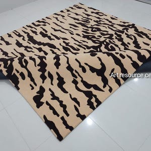 Puede incluir: Una alfombra beige y negra con un patrón de rayas de tigre. La alfombra está enrollada y se ve la parte inferior.