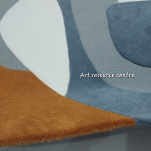 Puede incluir: Una alfombra redonda con un dise&ntilde;o abstracto moderno en tonos azules, blancos y marrones. La alfombra tiene una textura suave y mullida.