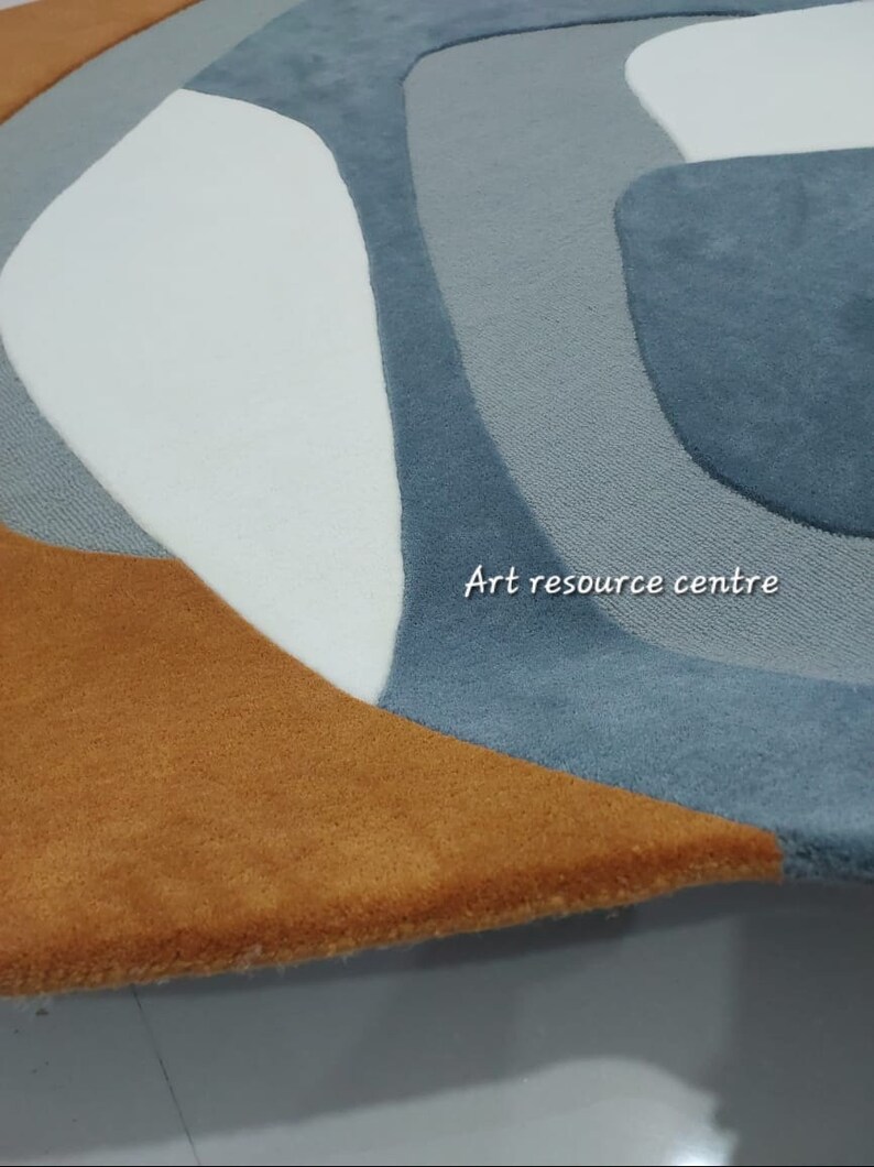 Puede incluir: Una alfombra redonda con un dise&ntilde;o abstracto moderno en tonos azules, blancos y marrones. La alfombra tiene una textura suave y mullida.