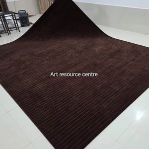 May include: A large, rectangular brown rug with a ribbed texture. The rug is folded over, revealing its underside. The text "Art resource centre" is printed on the rug.