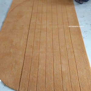 Puede incluir: Una alfombra grande, rectangular, de color marr&oacute;n claro con un borde curvo y l&iacute;neas verticales paralelas. La alfombra est&aacute; hecha de un material suave y es adecuada para una sala de estar o un dormitorio. El texto "Art resource centre" es visible.