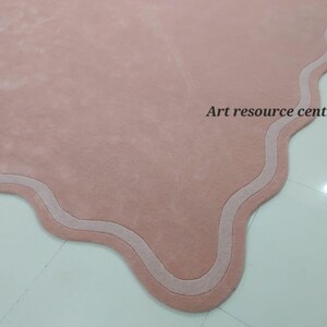 Puede incluir: Una alfombra rosa con un borde festoneado y un borde blanco. La alfombra est&aacute; hecha de un material suave y mullido.