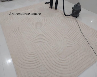 May include: A white rug with a geometric pattern of curved lines. The rug is being cleaned with a vacuum cleaner. The text "Art resource centre" is visible in the top left corner of the image.