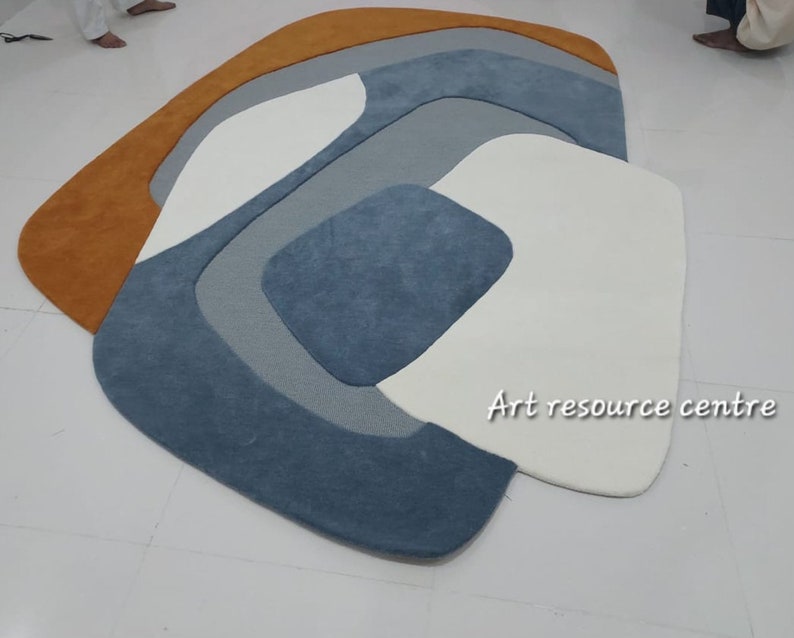 Puede incluir: Alfombra de &aacute;rea abstracta con un dise&ntilde;o moderno que presenta una combinaci&oacute;n de colores naranja, blanco, gris y azul. La alfombra tiene una forma org&aacute;nica &uacute;nica y una textura suave y mullida. "Art resource centre" est&aacute; escrito en texto blanco en la alfombra.