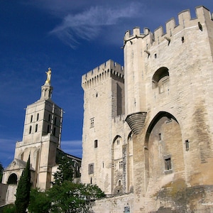 May include: A large, stone building with a tall tower and a statue on top. The building has a lot of windows and arches. The sky is blue and there are clouds in the sky.