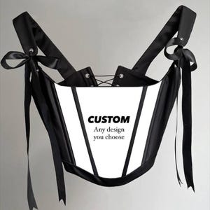 May include: A black and white corset with black straps and bows. The corset has a lace-up back and the text "CUSTOM Any design you choose" printed on the front. The corset is a fashion item.