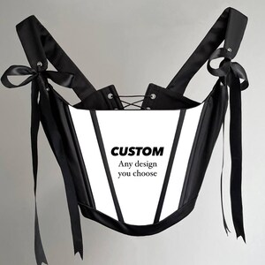 Puede incluir: Un cors&eacute; blanco y negro con correas y lazos negros. El cors&eacute; tiene un panel frontal blanco con el texto "CUSTOM Any design you choose". El cors&eacute; tiene una espalda con cordones.