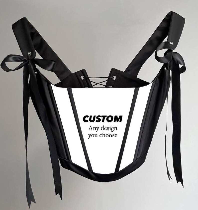 Puede incluir: Un cors&eacute; blanco y negro con correas y lazos negros. El cors&eacute; tiene un panel frontal blanco con el texto "CUSTOM Any design you choose". El cors&eacute; tiene una espalda con cordones.