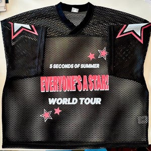 May include: Black mesh jersey with a V-neck collar. The jersey features the text "5 SECONDS OF SUMMER" above "EVERYONE'S A STAR! WORLD TOUR" in white and pink lettering. Pink star graphics and white and pink star accents are also visible.
