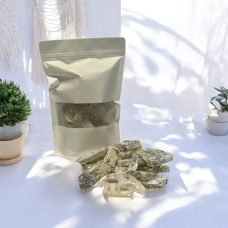 Pu&ograve; includere: Un sacchetto bianco richiudibile pieno di pezzi di caramelle trasparenti, scintillanti, verdi e bianche. Il sacchetto &egrave; su una superficie bianca con una piccola pianta in vaso sullo sfondo.