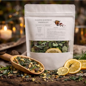 May include: A white pouch labeled "Cleanse & Refresh Simmer Pot" with ingredients and directions. A wooden scoop holds a mixture of herbs and spices. Sliced lemons and greenery are scattered around the pouch.