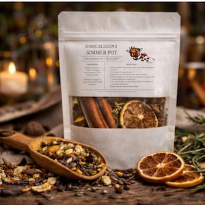 Puede incluir: Una bolsa transparente etiquetada como "Home Blessing Simmer Pot" llena de hierbas secas, especias, palitos de canela y rodajas de naranja. Una cuchara de madera contiene una mezcla de hierbas. Ingredientes: limón, naranja, salvia, romero, clavo y canela.