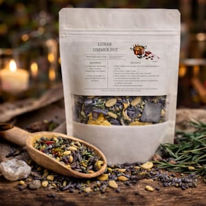 May include: A clear bag labeled "Lunar Simmer Pot" filled with dried herbs and spices. The bag includes ingredients and directions. A wooden scoop filled with herbs and spices sits in front of the bag on a wooden surface.