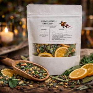 May include: A white pouch labeled "Summer Citrus Simmer Pot" with a clear window displaying dried orange slices, herbs, and spices. A wooden scoop filled with similar ingredients sits beside the pouch, along with fresh orange slices and bay leaves. The ingredients are for a simmer pot.