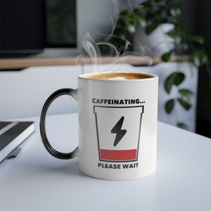 May include: White ceramic coffee mug with a black handle. The mug has a black and red graphic of a coffee cup with a lightning bolt and the text "CAFFEINATING... PLEASE WAIT".