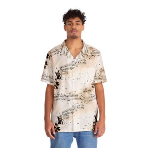 Könnte beinhalten: Kurzärmeliges Hemd in Cremefarbe mit einem Notenmuster. Das Hemd hat schwarze Noten und braune Akzente. Es hat einen klassischen Kragen und eine einzelne Brusttasche. Das Model trägt eine blaue Jeans.