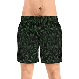 Könnte beinhalten: Schwarze Badeshorts mit einem sich wiederholenden Muster aus grünen Cannabispflanzenblättern. Die Shorts haben einen Kordelzug in der Taille und sind aus leichtem Material gefertigt. Das Design ist ein auffälliger Allover-Print.